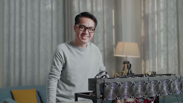 Asian Man Wearing Glasses Smiling To Camera While Using Laptop With Mining Cryptocurrency alt