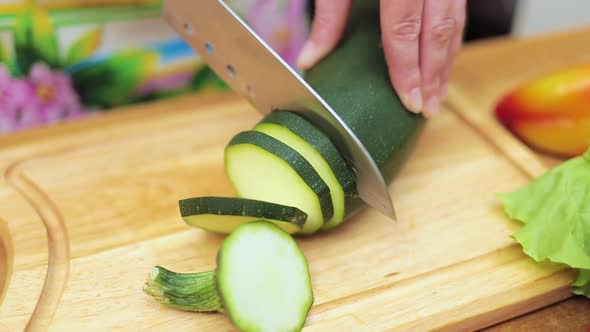 Women's Hands Housewives Cut with a Knife Fresh Zucchini on the Cutting Board of the Kitchen Table alt