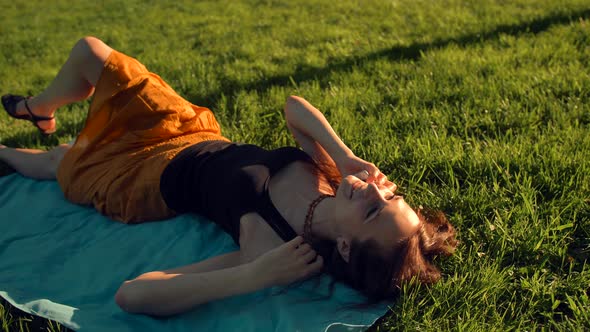 Smiling Young Woman Lying on the Grass and Talking By Phone. alt