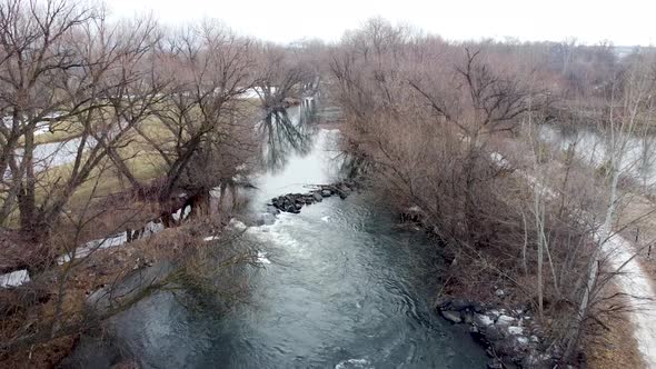 Small river dam and rapids on scenic, idyllic, willow tree lined flowing river in winter in rural co alt