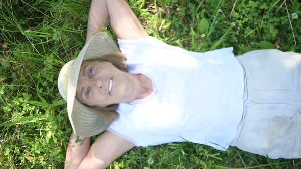Happy Smiling Elderly Senior Woman in Straw Hat Having Fun Lying on Grass Posing in Summer Garden