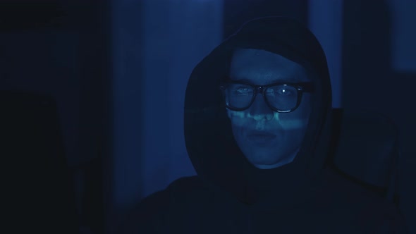 Portrait of Hooded IT Hacker Programmer Developer in Glasses Working Computer Cyber Attack on Server alt