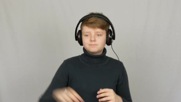Funny Teen Boy in Big Headphones on His Head is Listening to Music Dancing and Having Fun on a White