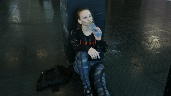 Happy Fitness Girl Sitting at Sport Club and Drinks a Water After Training