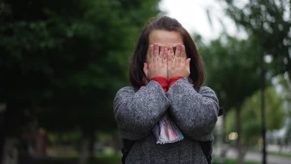 Young Caucasian Little Woman Closing Face with Hands Making Wish Standing Outdoors on Overcast Rainy alt