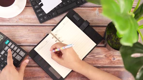 Top View of Women Hand Using Calculator and Writing on Notepad on Office Desk alt