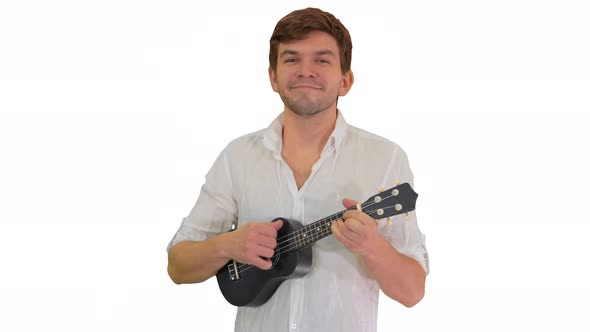 Smiling Young Man Playing Ukulele Looking Into the Camera on White Background alt