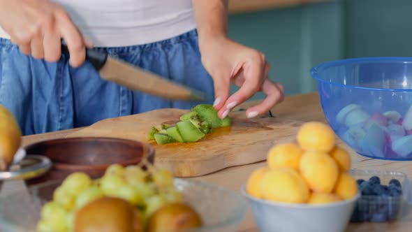 Closeup Of Female Hand Cutting Kiwi For Fruit Salad