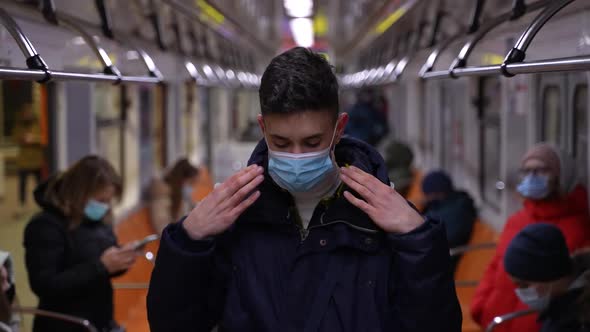 Tall Teen Boy Putting on Face Mask in Subway Train alt