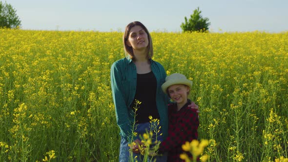 Mother Woman Stands in Yellow Flowering Rapeseed Embrace Little Daughter alt