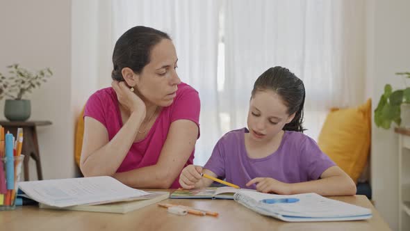 Mother helping her young daughter prepare homework during homeschooling alt