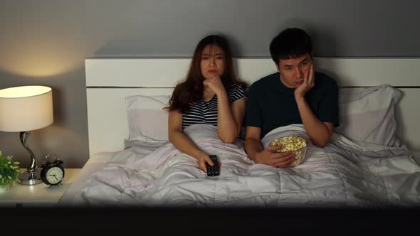 bored young couple watching TV on a bed at night