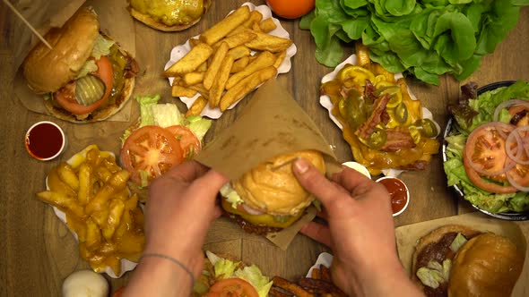 Serving Burger in a Paper Wrap on a Table Full of Fast Food Dishes alt