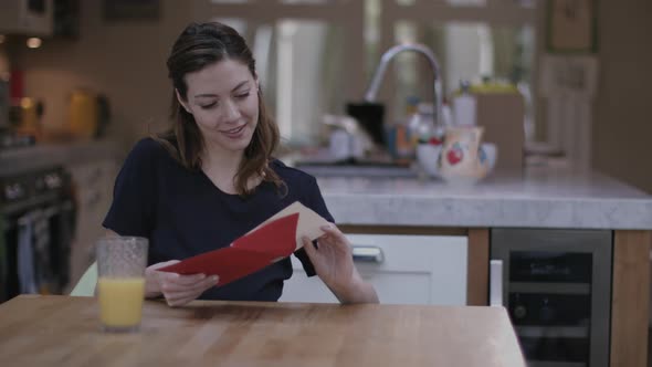 Young adult female opening Valentine's Day Card at Kitchen table