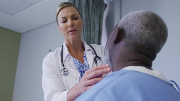 Caucasian female doctor examining neck of african american senior male patient at hospital alt