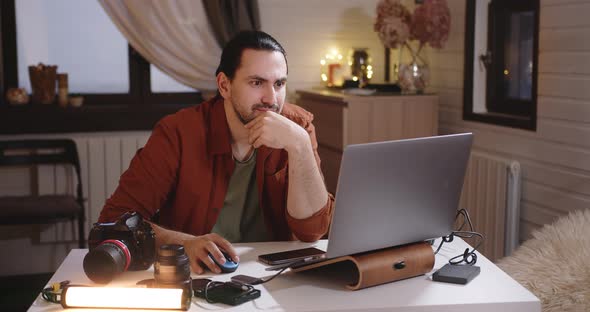 A Young Handsome Male Photographer and Videographer Works at Home on a Laptop alt