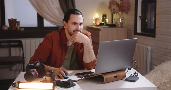 A Young Handsome Male Photographer and Videographer Works at Home on a Laptop