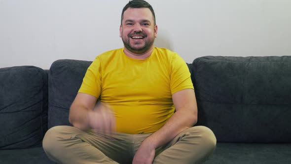 Man in Yellow Tshirt Waves His Hand in Greeting to the Camera and Tells Something
