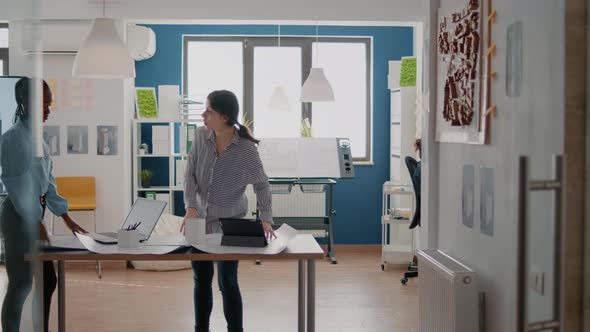 Multi Ethnic Team of Women Using Tablet and Blueprints Plans to Design Building Layout and Structure alt