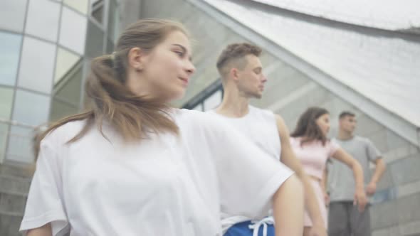 Portrait of Four Joyful Caucasian Young Dancers Standing in a Row on Urban Stairs and Moving Hands alt