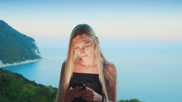 Blonde Woman Using Smartphone with Ocean in the Background alt