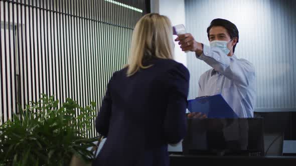 Caucasian businessman wearing face mask checking coworkers temperature alt