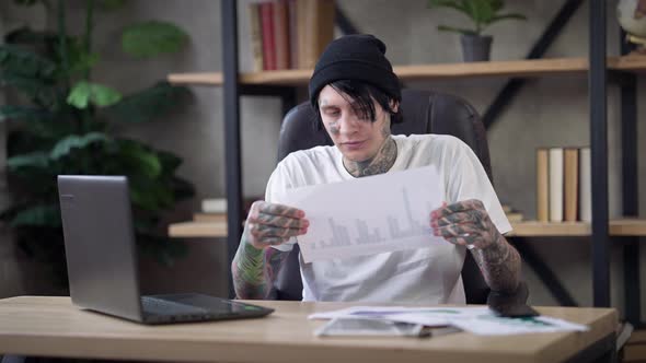 Troubled Male Tattooed Analyst Tearing Paperwork Thinking Sitting in Home Office on Covid19 Pandemic alt
