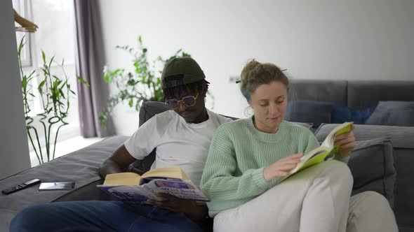 Young Mixed Couple Sitting on Their Couch and Reading Books alt