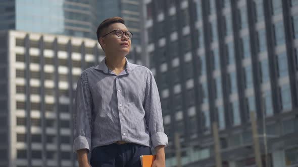 Portrait handsome Asian businessman holding a book standing looking around the urban city.