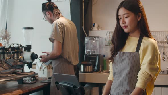 Young Asia female barista taking order by mobile phone and digital tablet standing behind alt