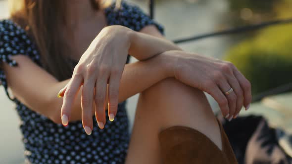 Closeup of the Hands of a Young Girl Sits on a Suspension Bridge at Sunset