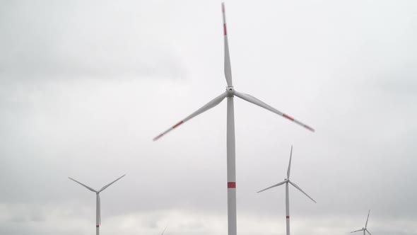 Motion the Blades of a Large Wind Turbine in a Field Against a Background of Cloudy Grey Sky on the alt