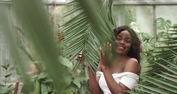 Portrait of a Beautiful Young Girl in a Greenhouse Smiling and Looking at Camera alt