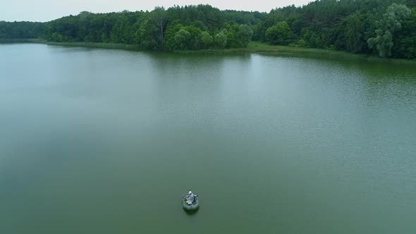 Aerial View Fisherman is Fishing Sitting on an Inflatable Boat in Middle of Lake alt