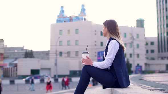 Attractive Girl in the Evening in the City Center, in a Business Suit, Drinking Coffee and Holding