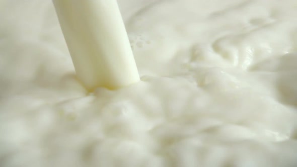 A pouring stream of milk into the milky surface. Slow motion. alt