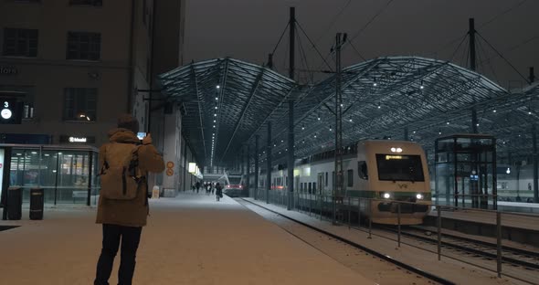 Train leaving the station at night and man making video on mobile alt