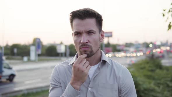 A Young Caucasian Man Thinks About Something in an Urban Area  Busy Intersection in the Background alt
