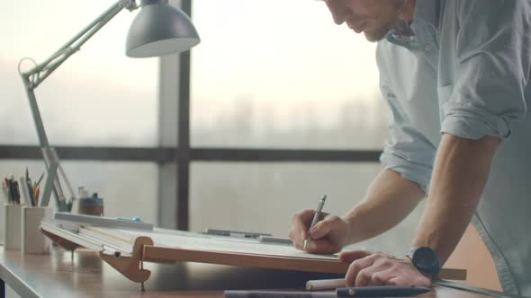 Engineer Draws Buildings on the Table Using a Pencil and Ruler alt