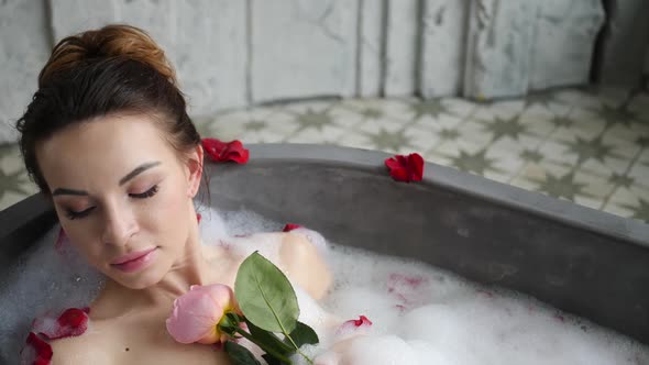 Sexy Girl Lies in a Big Stone Bath with a Rose Flower in Her Hands alt