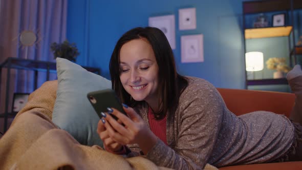 Woman Lying on Sofa at Home Using Mobile Phone Communicating in Social Network or Online Shopping alt