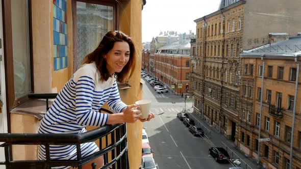 Young Woman Drinking Hot Coffee on Balcony and Observing Cityscape in Downtown