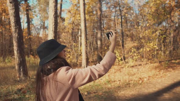 Young Blogger Girl Is Filming Herself By Phone on Walk in Autumn Forest alt