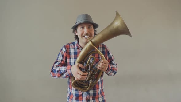 Cheerful Young Man with a Funny Mustache and a Hat Playing on the Big Tuba. 