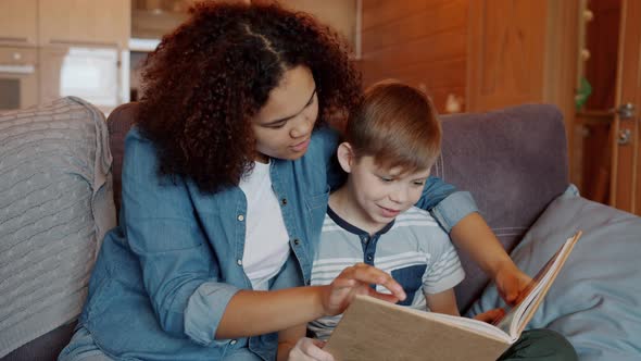 Slow Motion of Caring Afro-American Babysitter Reading Book To Smart Kid at Home alt