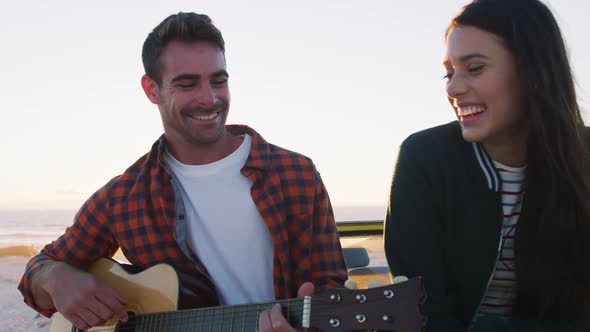 Happy caucasian couple sitting in beach buggy by the sea playing guitar alt