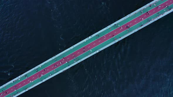 The Movement of People on a Footbridge Over a Large River with Dark Blue Water  Top Down Shot alt