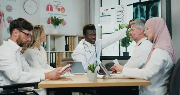 Multicultural Male and Female Doctors Holding Joint Council in Modern Workroom in Clinic alt