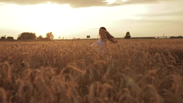 Beautiful Young Woman Enjoys Life Walking on a Wheat Field at Sunset