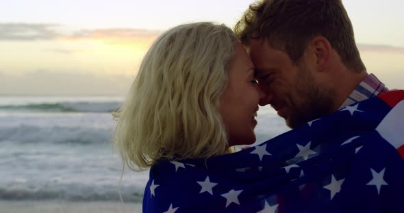 Couple wrapped in american flag at beach during sunset 4k
